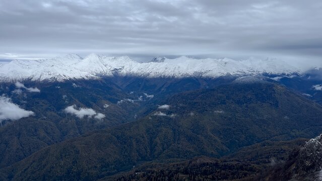 Panoramic View of Snow-Capped Mountains Above Forest Valley Under Cloudy Sky