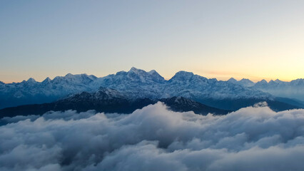 Jagged snowy mountain peaks rising above a thick layer of white clouds at dawn