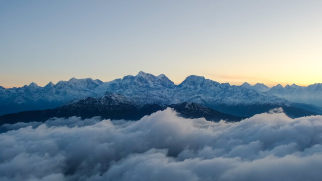Jagged snowy mountain peaks rising above a thick layer of white clouds at dawn