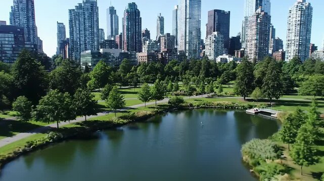 High-altitude aerial drone video of gleaming modern skyscrapers, lush urban park with tranquil ponds, and sparkling blue water. Concept of urban innovation and natural serenity