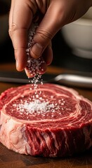 Chef sprinkles coarse salt crystals onto a thick cut of uncooked red meat