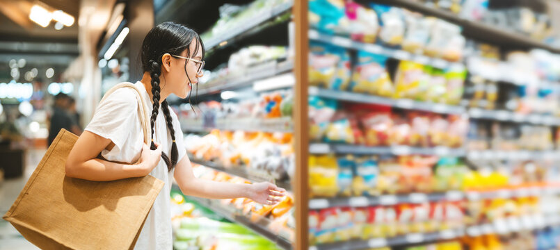 Young adult asian woman customer choosing snack food from shelf shopping at asia supermarket