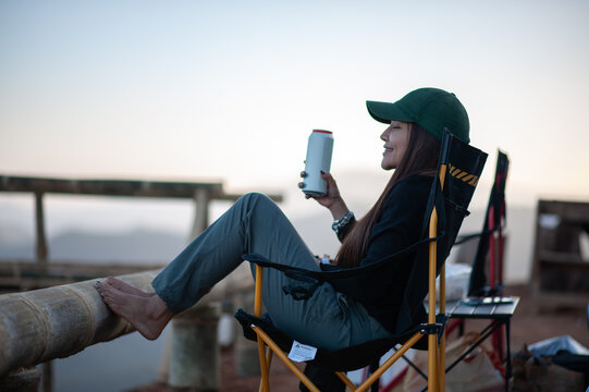 A woman sits holding a canned drink in the middle of nature.