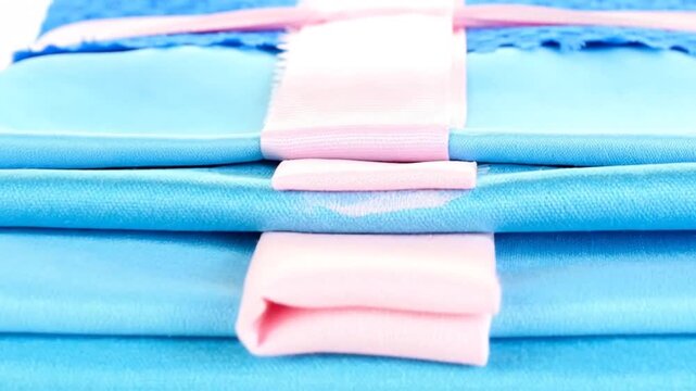 A stack of textured, folded fabrics in shades of blue and pink, bound with pink ribbon