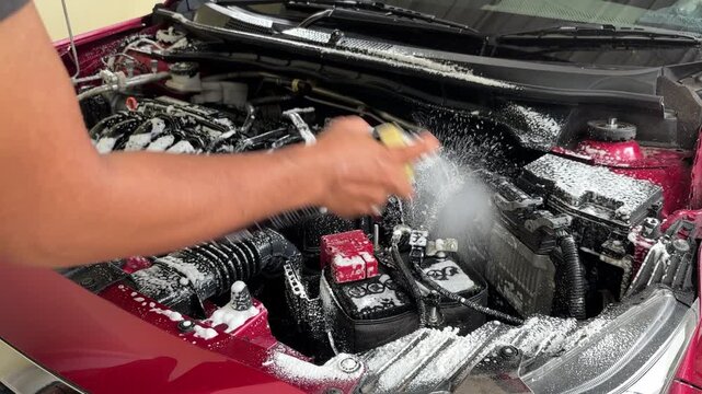 The process of cleaning the car engine compartment by spraying foam liquid into the dirty and dusty engine compartment.