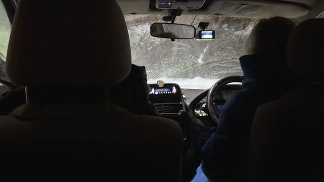 Woman driving a car at night from back seat perspective. Car interior view with dashboard camera and frosty windshield, winter road trip concept. Snowy forest ride.