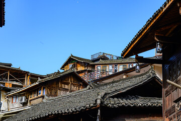 Fototapeta premium A traditional Miao village building in Guizhou, showcasing the distinct brownish-yellow fir timber framework and the layered gray ceramic roof tiles, embodying the rustic architectural style.