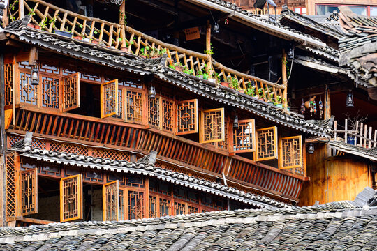 A traditional Miao village building in Guizhou, showcasing the distinct brownish-yellow fir timber framework and the layered gray ceramic roof tiles, embodying the rustic architectural style.