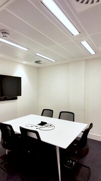 Empty meeting room with table, chairs, TV screen, and conference phone. vertical video