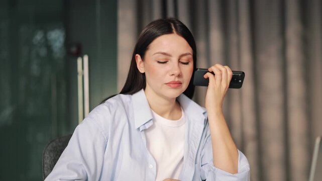 Focused woman listens to smartphone audio, holding device near ear. Displays concentration and thoughtfulness while receiving information. Modern communication moment.