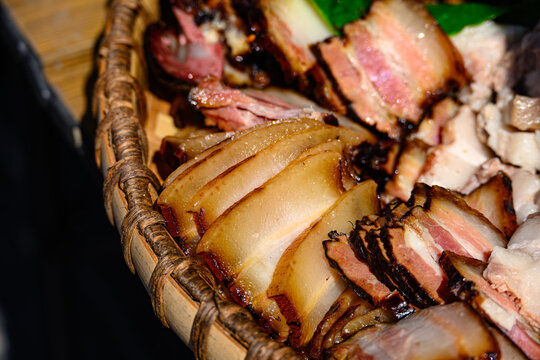 Thin slices of traditional Miao cured pork are arranged on a woven bamboo tray, glistening translucently under the sunlight highlighting the rich fat marbling and the appetizing amber hue of the meat.