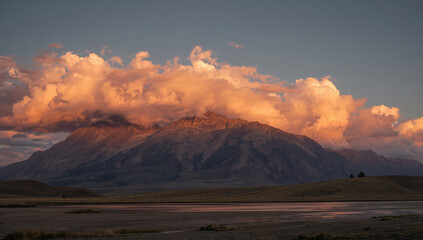 Majestic mountain sunrise cloud glow over rugged peak with reflective lake shore