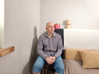 Thoughtful man in a striped shirt sitting on a chair looking right. Pondering and calm emotion. Candid portrait for emotional concept