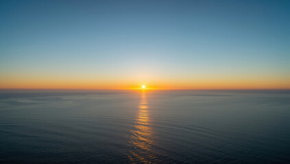Fototapeta premium Serene ocean sunset with sun reflecting on calm water and soft gradient sky