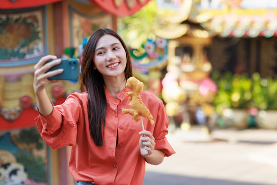 Young asian woman holding a dinosaur shaped snack taking selfie
