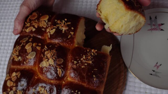 Hands breaking a piece of baked brioche bread filled with lemon curd, placing it on a plate and slicing with a knife. Close-up homemade pastry serving process, lemon filling visible inside.