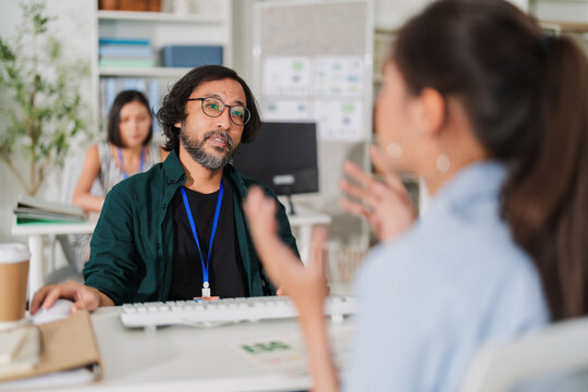 Three cheerful Asian coworkers gather around a laptop in a modern office, smiling and celebrating teamwork and success while reviewing documents together in a bright, creative, and supportive work env
