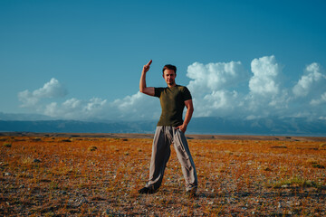 Young european man standing in steppe with clouds, one hand up, one hand in pocket