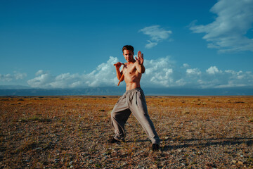Young athletic man practicing nunchaku in steppe, martial pose