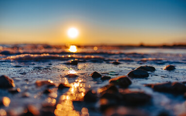 Close-up macro of pebbles on shore with waves and sunset reflected in water