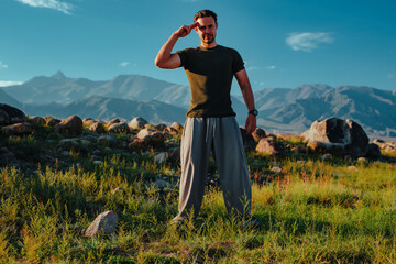 Athletic young man saluting outdoors with mountains in background