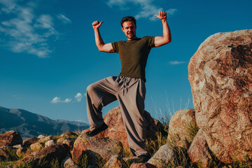 Motivated young man showing thumbs up with both hands on rocks