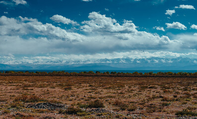 Steppe view of Kyrgyzstan with mountains, lake and clouds on bright sunny day