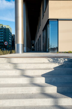 Empty urban plaza with concrete steps and columns sits beside a modern building as shadow shapes architecture into clean open space