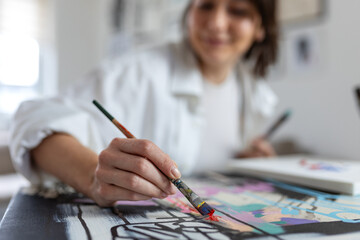 Close-up of artist painting on canvas with paintbrush and red oil paint. Focused view of creative process and brushstrokes in bright art studio. Hand of professional painter creating artwork.