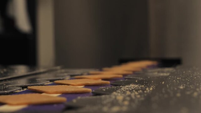 Static close-up shot of square sugar candies on a stainless-steel machine surface as a hand enters the frame to place the candies into the confectionery production line.