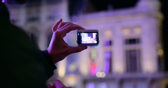 A person is holding a white action camera at night in a city The illuminated building in the background suggests travel vlogs content creation and capturing memories.