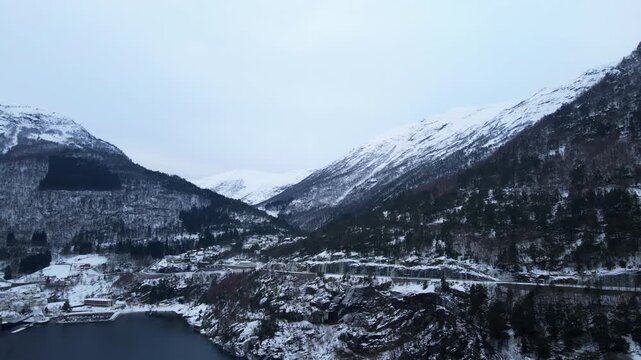 Scenic drone shot of Hellesylt, a small town in Norway surrounded by fjords and tall mountains and snow covering the landscape on a bright winter day