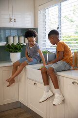 Obraz premium Diverse siblings handling fresh bell pepper and chatting on countertop beside farmhouse-style sink