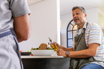 Couple preparing fresh salad at kitchen island, pouring olive oil into lettuce and tomato © wavebreak3