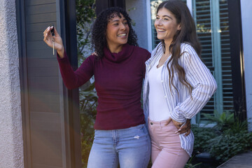 Diverse female friends with silver house keys and smiling in front of home entrance