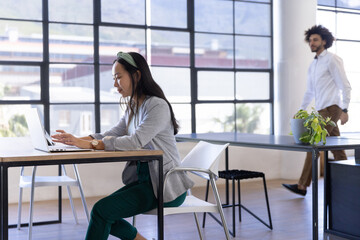 Laptops are sitting on wooden desks while white chairs are framing grid windows in office