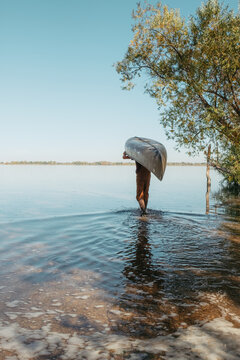 Man portaging canoe through water at summer lake