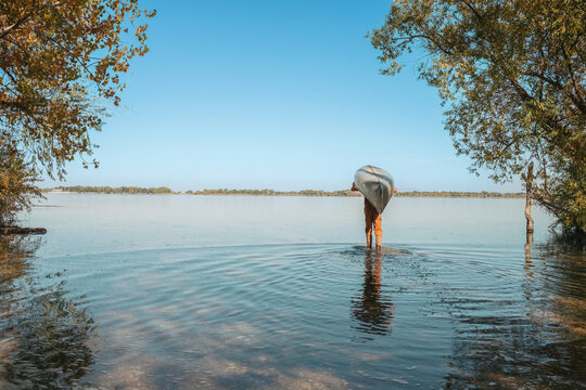 Person walking into summer lake carrying a canoe