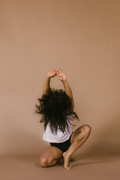 Black woman with curly hair and arms above head in dance pose