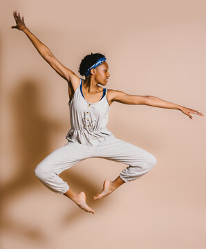 Black female dancer does a leap in studio neutral background