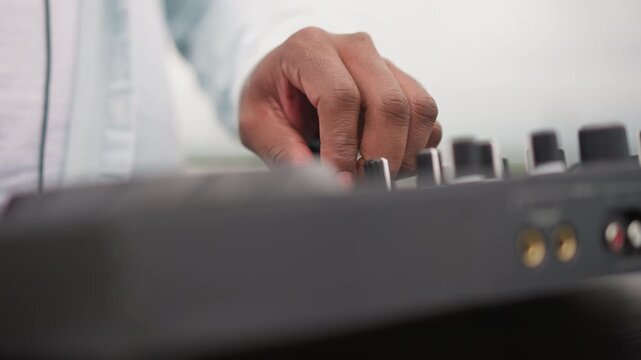 closeup dj hands on controller adjusting knobs and sliders, white shirt sleeve visible, gold audio ports on front panel, shallow depth of field, steady rhythmic motion, urban street musician vibe