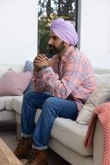 Obraz premium Indian man with turban sitting on sofa in living room looking through window