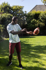 African american man catching american football on manicured backyard lawn