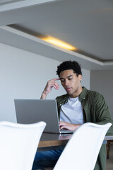 African american man sitting at table in room using laptop under recessed ceiling light