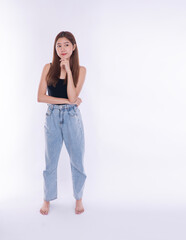 Thoughtful Asian woman standing barefoot black tank top baggy jeans. Pensive female touching chin looking aside copy space, making decision solving problem on white background.Lifestyle choice concept