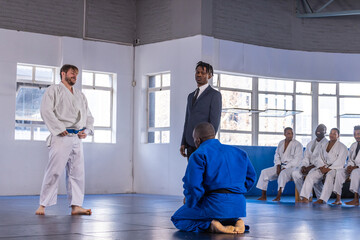 Diverse martial arts students sparring in white, blue gis with blue belt on dojo mats