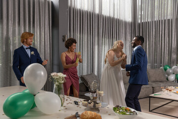 Naklejka premium Diverse couple dancing and laughing in decorated reception hall with balloons, cupcake stand