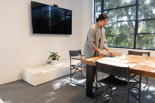 Woman standing by wooden table in meeting room arranging tablet near glasses, copy space