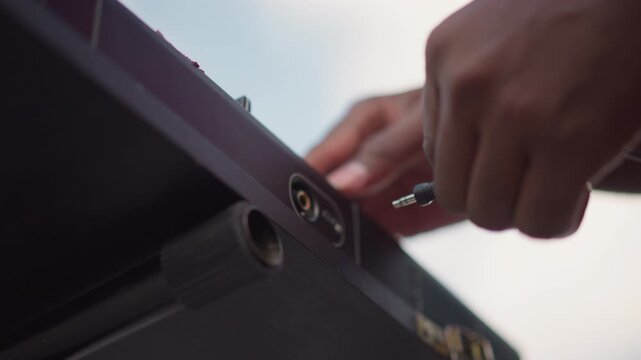 hands unplugging audio cable from speaker, street DJ packing gear after outdoor set, closeup of jack removal, dusk sky, empty stage and calm reflective mood, roadie tending flightcase