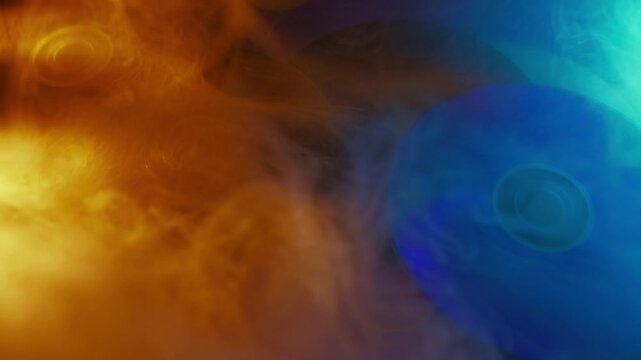Vibrant cds surrounded by swirling orange and blue smoke transform through light and shadow